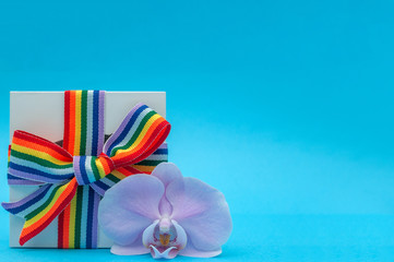 white gift box with rainbow ribbon and Orchid flower on blue background