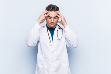 Young handsome doctor man touching temples and having headache.