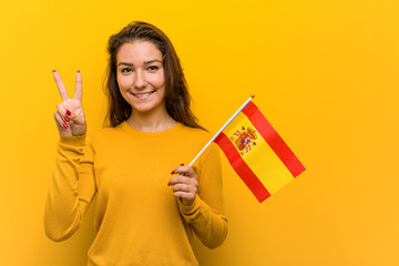 Young european woman holding a spanish flag showing number two with fingers.