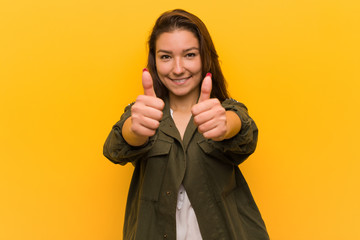 Young european woman isolated over yellow background with thumbs ups, cheers about something,...