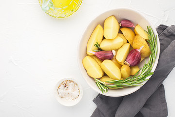Slices of raw fresh potatoes before cooking with basil, rosemary, butter, garlic and salt for baking in country style. Top view in horizontal. Comfortable healthy food for the whole family.