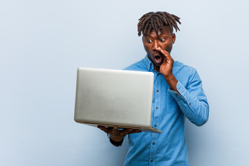 Young rasta black man holding a laptop shouting excited to front.