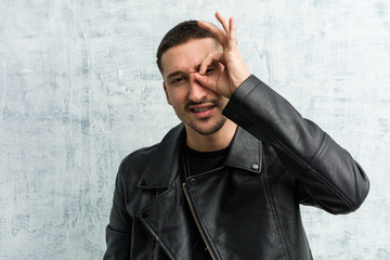 Young rocker man excited keeping ok gesture on eye.