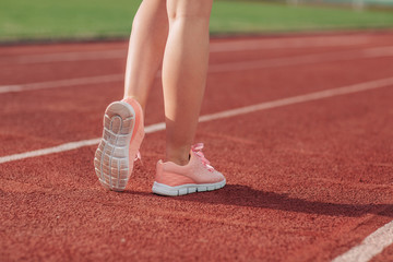 Girl legs in sport shoes standing on a running track with stadium stands. back view. close up