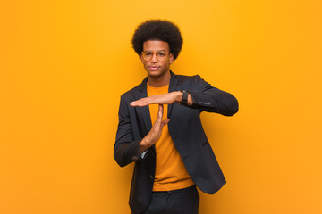 Young business african american man over an orange wall doing a timeout gesture