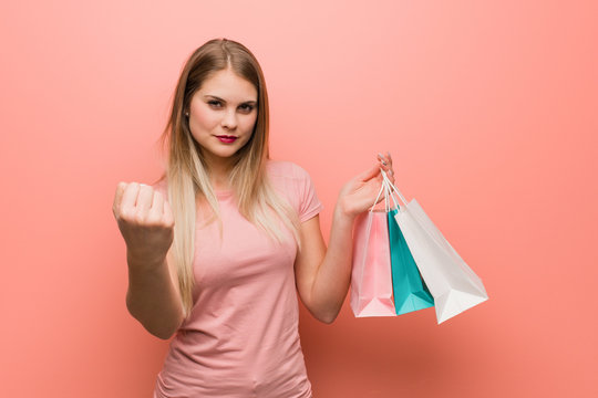 Young Pretty Russian Girl Showing Fist To Front, Angry Expression. She Is Holding A Shopping Bags.