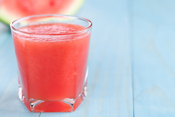Refreshing watermelon juice on blue wood, copy space on the right side (Selective Focus, Focus on the front of the glass rim)