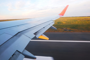 View from the porthole - Wing of an airplane taking off above the runway at high speed during the sunset. The land is running under the wing