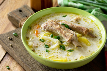 Vegetable soup with cabbage, sour cream and meat ribs on a kitchen wooden table.