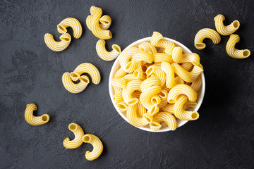 Bowl with raw pasta cavatappi on black background. Top view.