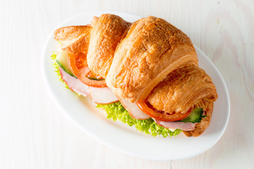 Fresh croissant or sandwich with salad, ham, jamon, prosciutto, salami, cheese, chicken, tomatoes on wooden background. Morning breakfast concept. Healthy and fast food.