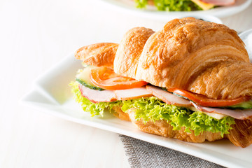 Fresh croissant or sandwich with salad, ham, jamon, prosciutto, salami, cheese, chicken, tomatoes on wooden background. Morning breakfast concept. Healthy and fast food.