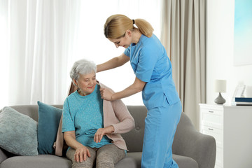 Nurse covering elderly woman with blanket indoors. Assisting senior people