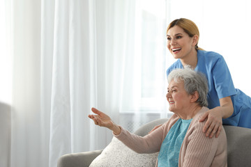 Nurse with elderly woman indoors, space for text. Assisting senior people