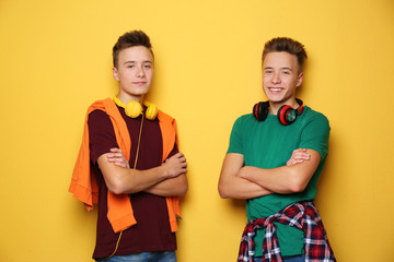 Teenage twin brothers with headphones on color background