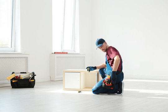 Handyman in uniform assembling furniture indoors. Professional construction tools