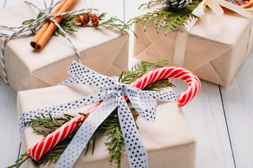 Gift boxes wrapped in wrapping paper with ribbons, pine cones and dried oranges on a white wooden background