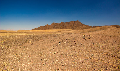 wasteland desert scenery landscape photography of sand stone dry valley foreground and mountains background in warm sunny weather time  
