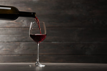 Fototapeta na wymiar Pouring red wine into glass from bottle on table against wooden background. Space for text