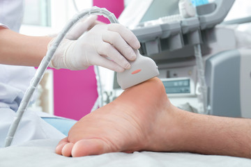 Doctor conducting ultrasound examination of patient's foot in clinic, closeup