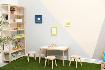 Stylish playroom interior with table, stools and green carpet