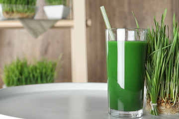 Glass of juice and sprouted wheat grass on table. Space for text