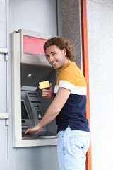 Fototapeta na wymiar Young man using cash machine for money withdrawal outdoors