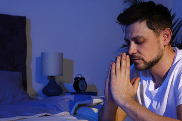Fototapeta premium Handsome man saying bedtime prayer in dark room at night. Space for text