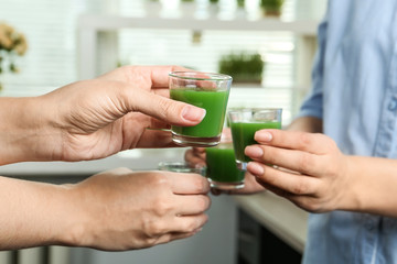 Women with shot glasses of wheat grass juice indoors, closeup