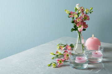 Composition with burning candles and flowers on grey marble table against color background, space for text