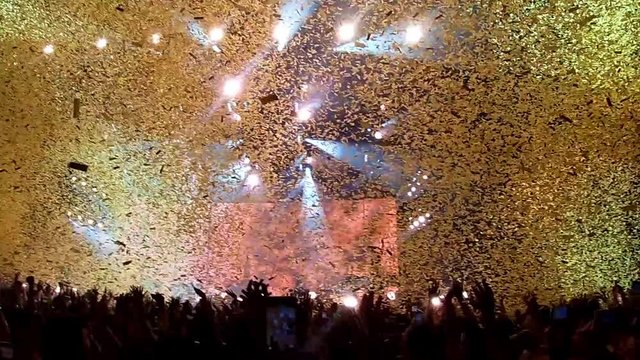 Gold confetti explosion floating in the air during a concert. Crowd cheering hands in air during a party.