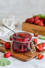 A jar of strawberry jam on a wooden board on a marble background 