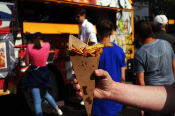 Fototapeta premium Organic french fries on street food festival in hand. Pulled pork or burger are sold on Open kitchen food festival event. Street food