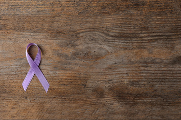 Purple ribbon on brown wooden background, top view with space for text. Domestic violence awareness