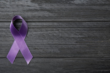 Purple ribbon on grey wooden background, top view with space for text. Domestic violence awareness