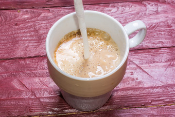 Milk is poured into a cup of coffee on a burgundy-colored wooden background.