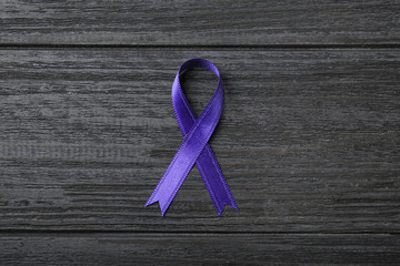 Purple ribbon on grey wooden background, top view. Domestic violence awareness