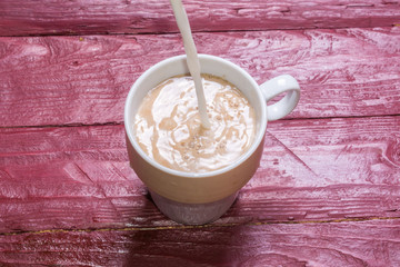 Milk is poured into a cup of coffee on a burgundy-colored wooden background.