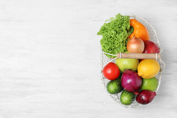 Basket with ripe fruits and vegetables on white wooden table, top view. Space for text