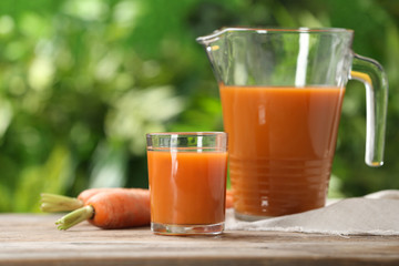 Glass and jug of carrot drink on table against blurred background, space for text