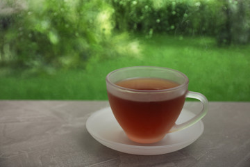 Cup of hot tea on brown windowsill, space for text. Rainy weather