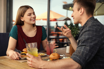 Young happy couple with burgers in street cafe