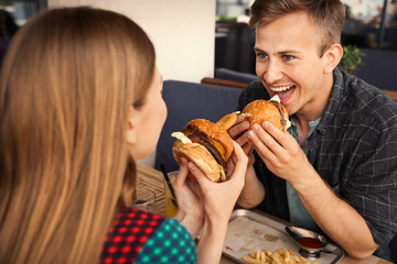 Young couple eating burgers in street cafe