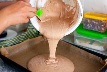 Woman hands with spatula putting chocolate dough on baking tray.