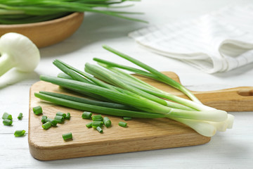 Wooden board with cut fresh green onions on white table