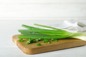 Wooden board with cut fresh green onions on white table. Space for text