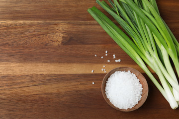 Obraz na płótnie Canvas Fresh green onions and bowl of salt on wooden background, top view. Space for text