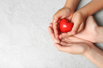 Woman and child holding heart on grey stone background, top view with space for text. Donation concept
