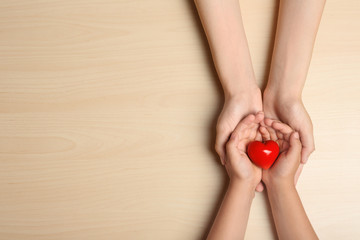 Woman and child holding heart on beige wooden background, top view with space for text. Donation...