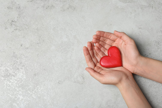 Woman holding heart on grey stone background, top view with space for text. Donation concept